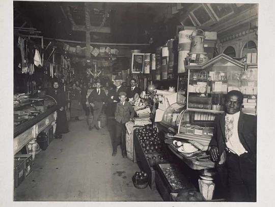 Black-and-white photograph of the crowded interior of Henry Gwinner’s store, with shelves, counters and men standing among the merchandise