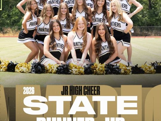 A cheerleading squad in matching uniforms poses together on a gym floor