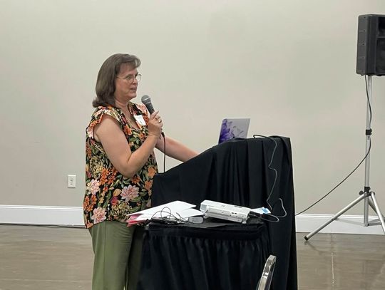 A woman speaks into a microphone at a podium during a conference session