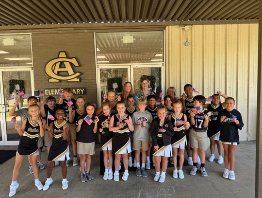 Fourth-grade students in matching school shirts hold small American flags during a Constitution Day visit