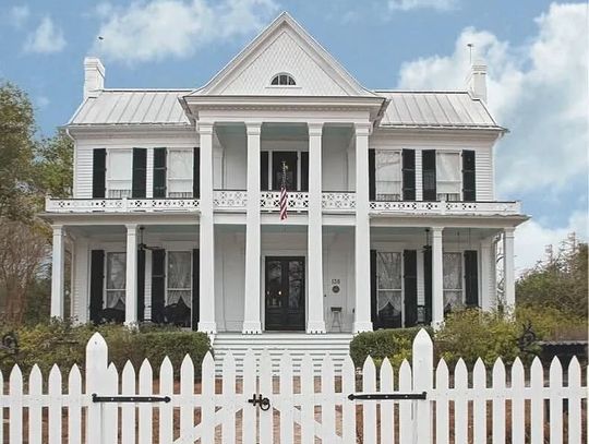 A white two-story antebellum house with tall columns and a white picket fence under a blue sky