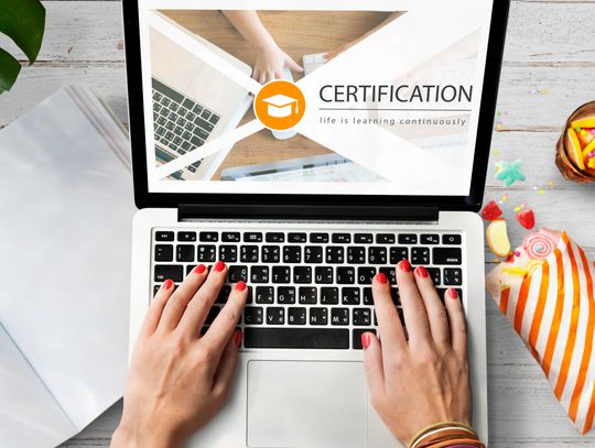 female with red nails using laptop with certifcation on the screen and snacks on table
