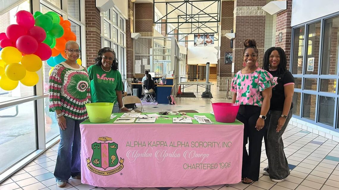 CPSD thanks Alpha Kappa Alpha chapter for voter registration efforts Women in pink and green stand behind a pink table with an Alpha Kappa Alpha banner and colorful balloons in a school lobby