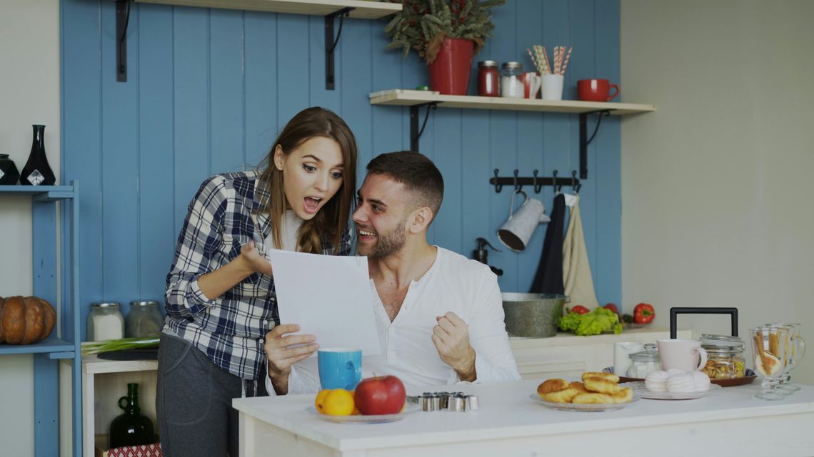 Essential Digital-Age Money Management Strategies for Busy Modern Families couple sitting in the kitchen looking at a paper surprised