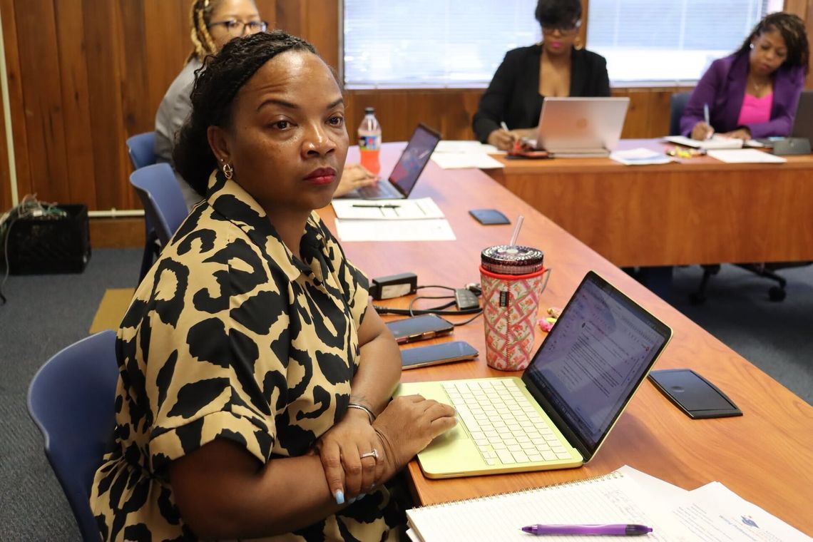 MDE conducts new writing standards professional development A woman in a leopard-print top sits at a conference table with a laptop and notepad while other attendees sit behind her