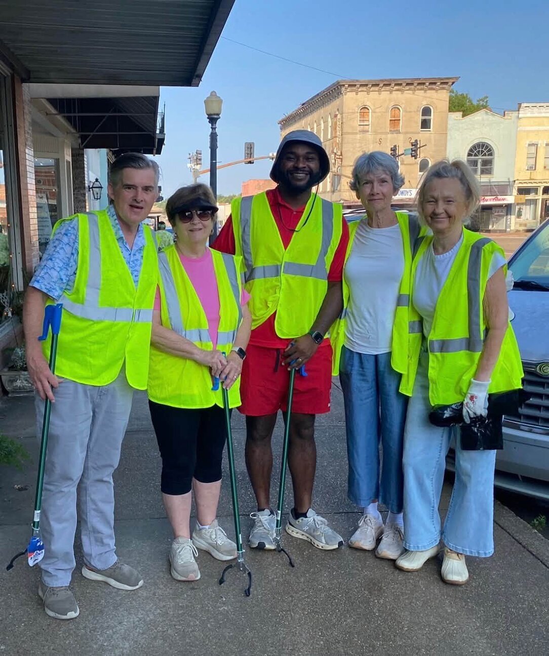 Five volunteers in safety vests with litter grabbers stand on a sidewalk along a downtown Canton street