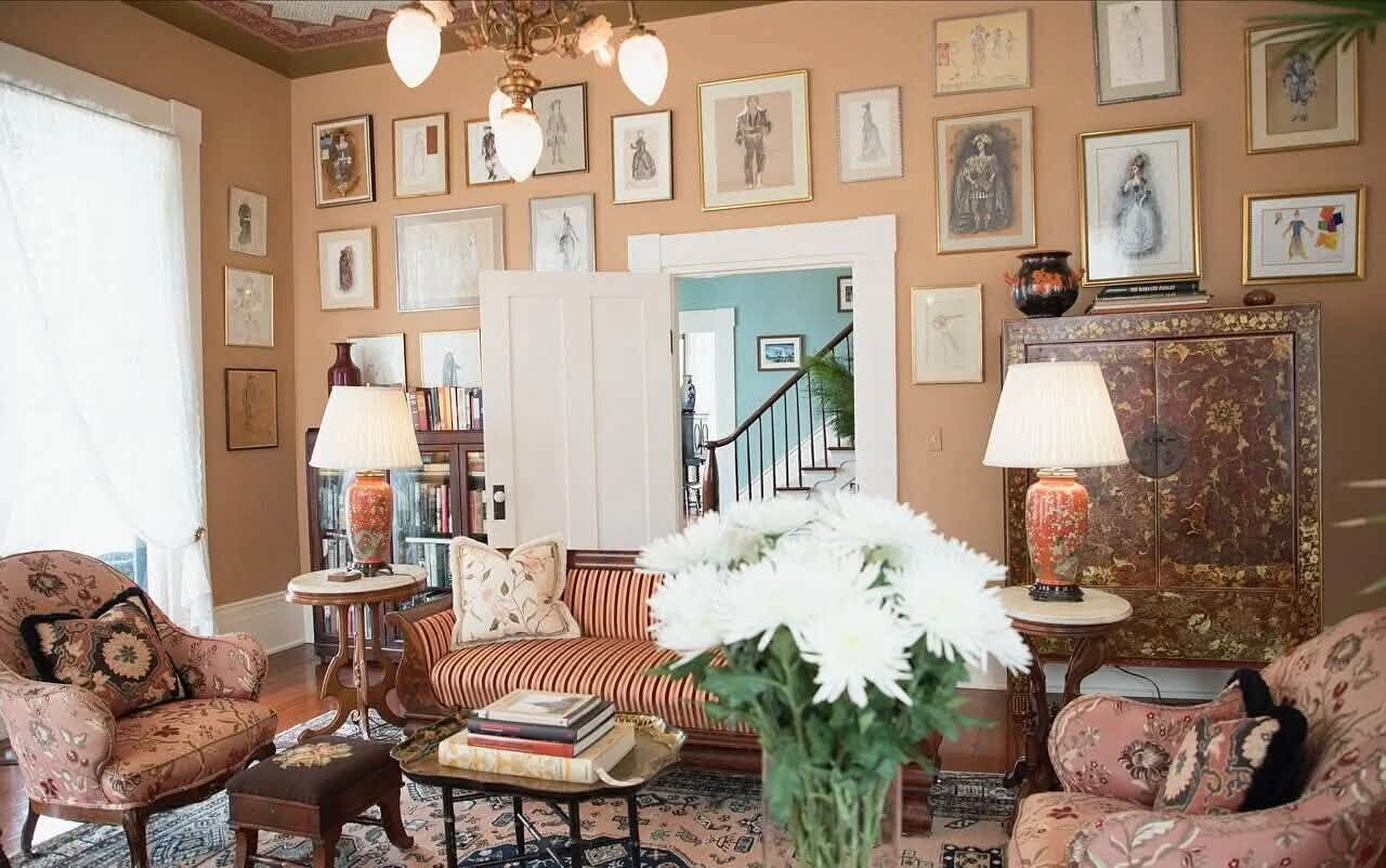 A formal living room with a patterned sofa, armchairs, a coffee table with white flowers, and framed pictures on the walls